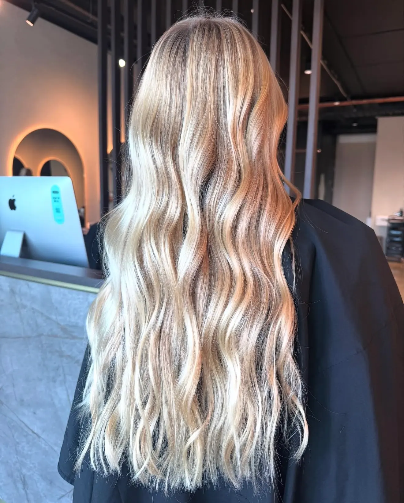 Long golden lived-in blonde waves with a soft root, photographed at the reception desk at Jenna Ellen Hair in Silverdale