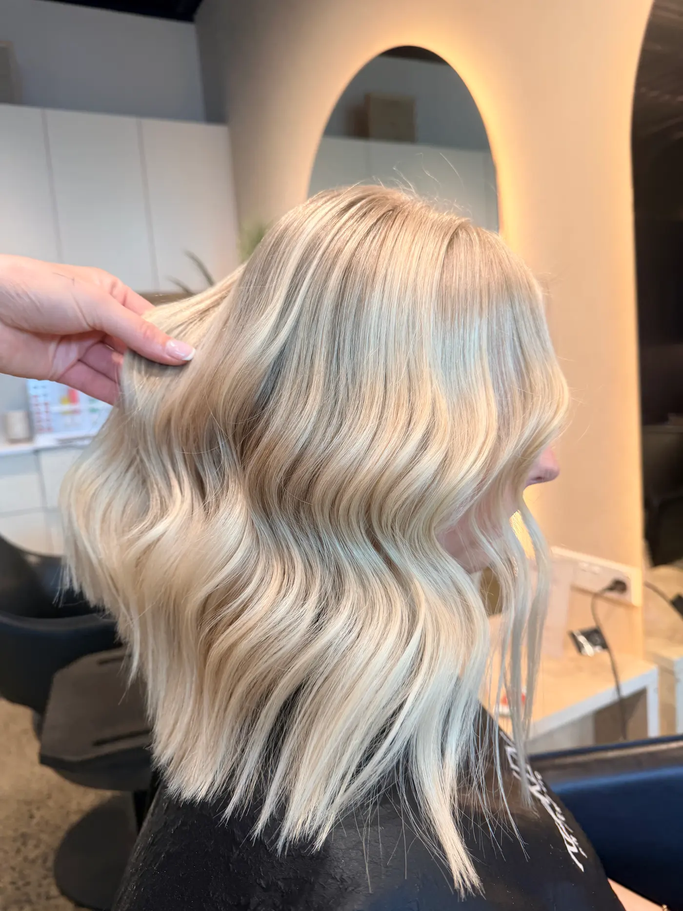 Icy blonde lob with soft waves, in front of the arched mirror