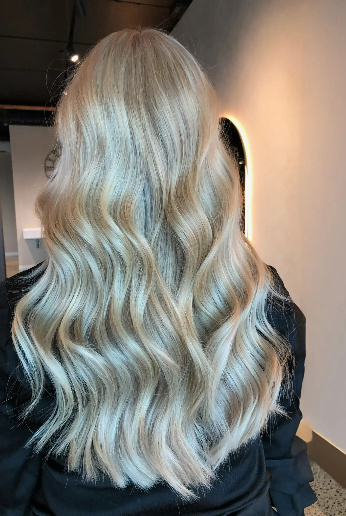Long icy blonde waves from the back, in front of the arched mirror